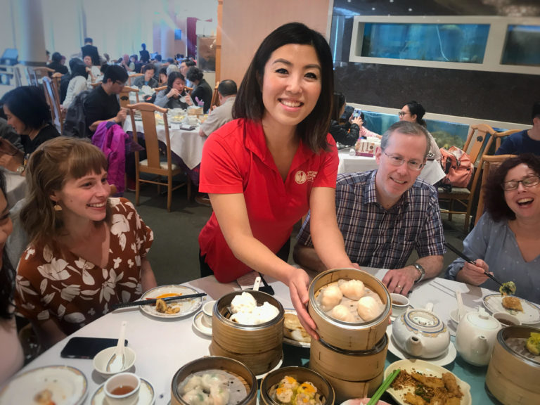 Tour guide Michelle smiling while showing food; tour guests laughing in background