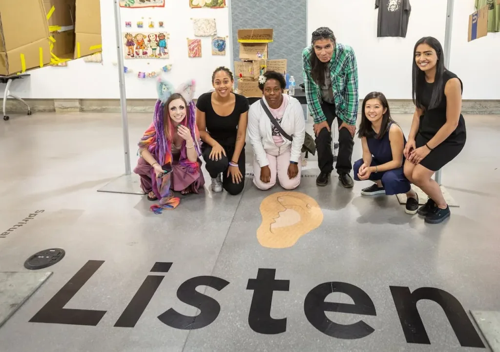 Small group of Employ to Empower workers and entrepreneurs pose for a photo in front of "LISTEN" stamped on the floor