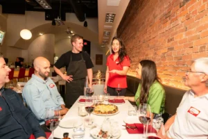 Vancouver Foodie Tour guide standing in front of a table where her guests on a Vancouver foodie tour are seated and listening to her explain the context behind the food they are about to try
