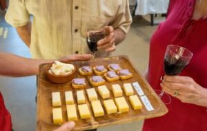 a tray of 3 different cheese tastings with two people holding red wine