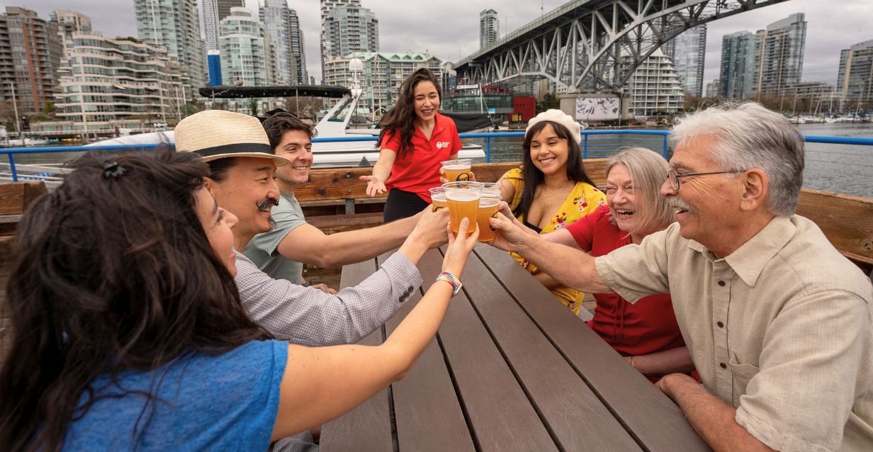 A foodie tour guide smiles as her group on Granville Island cheerses with beers with the Burrard Bridge in the background