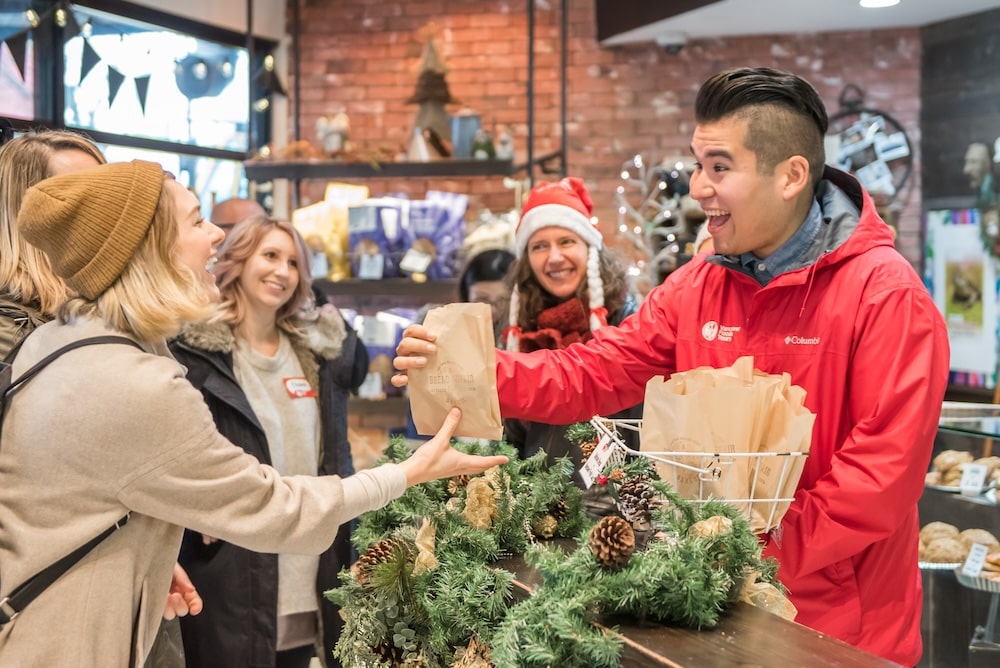 A Vancouver Foodie Tours guide handing out festive goodies in paper backs to his group of guests on the Festive Favorites Market Tour