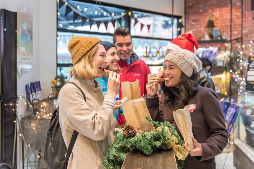 A group of smiling tourists pulling out Christmas goodies out of their paper bags and trying them out during the festive market tour in Vancouver