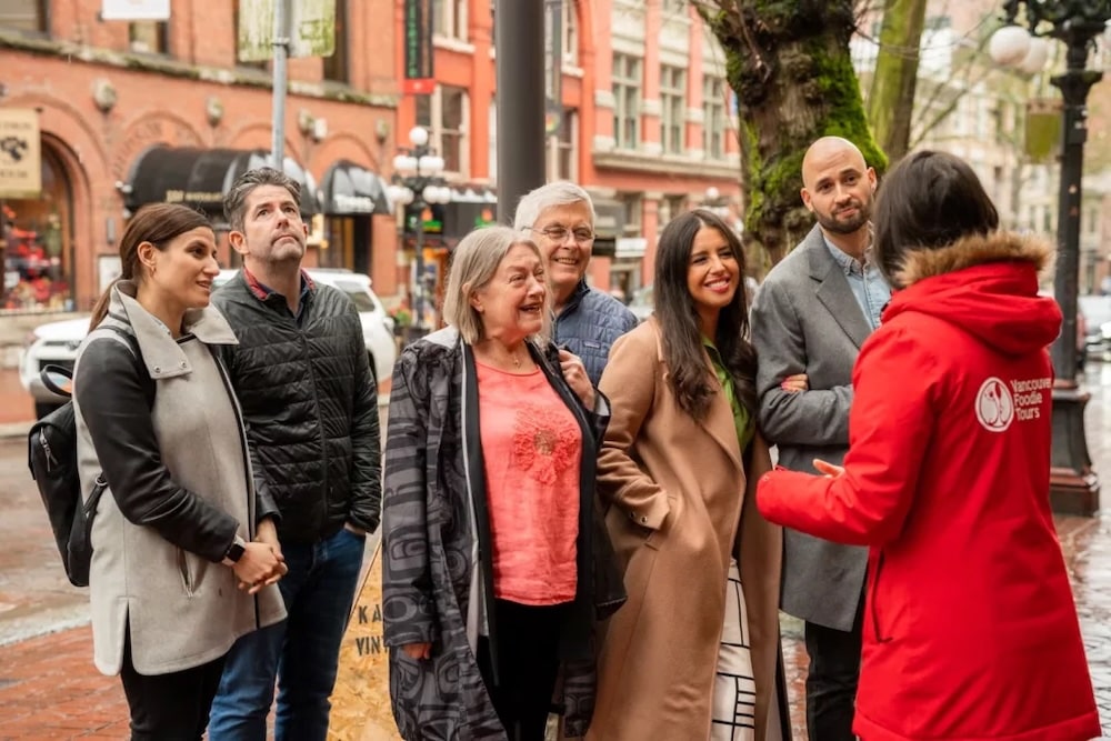 a guide in a red jacket standing in front of her group of guests who listen to her stories and smile at her