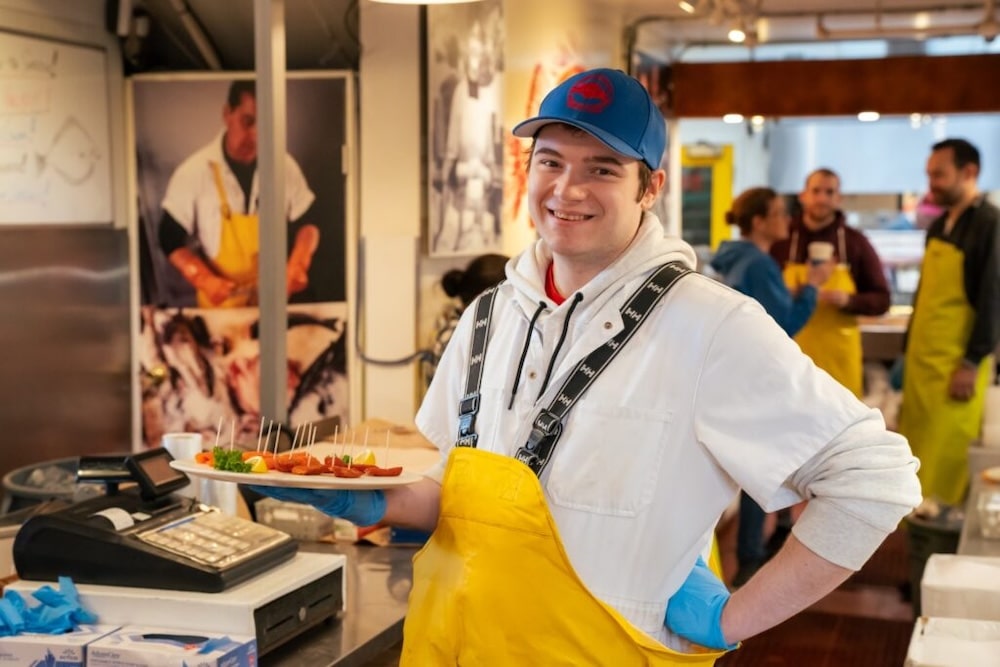 a fishmonger from Granville Island smiles at the camera as he holds a platter of local salmon