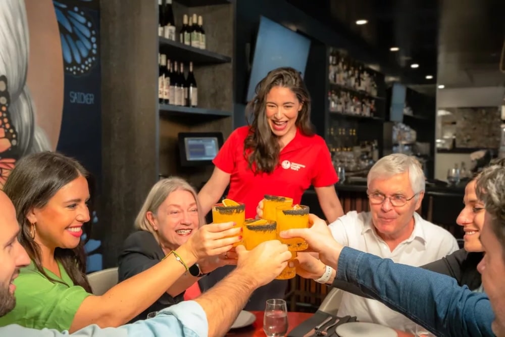 a Vancouver Foodie Tours guide watching as her group of guests raises their cocktail glasses to a common cheer