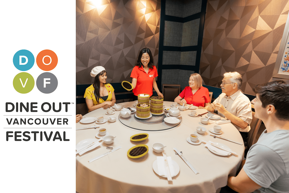 A tour guide standing at a table with guests seated around, revealing plates of delicious looking Asian cuisine