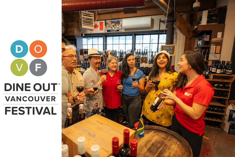 a tour guide standing in fron of a group of travelers in a wine shop holding a wine bottle and showing it to the group while explaining where it comes from