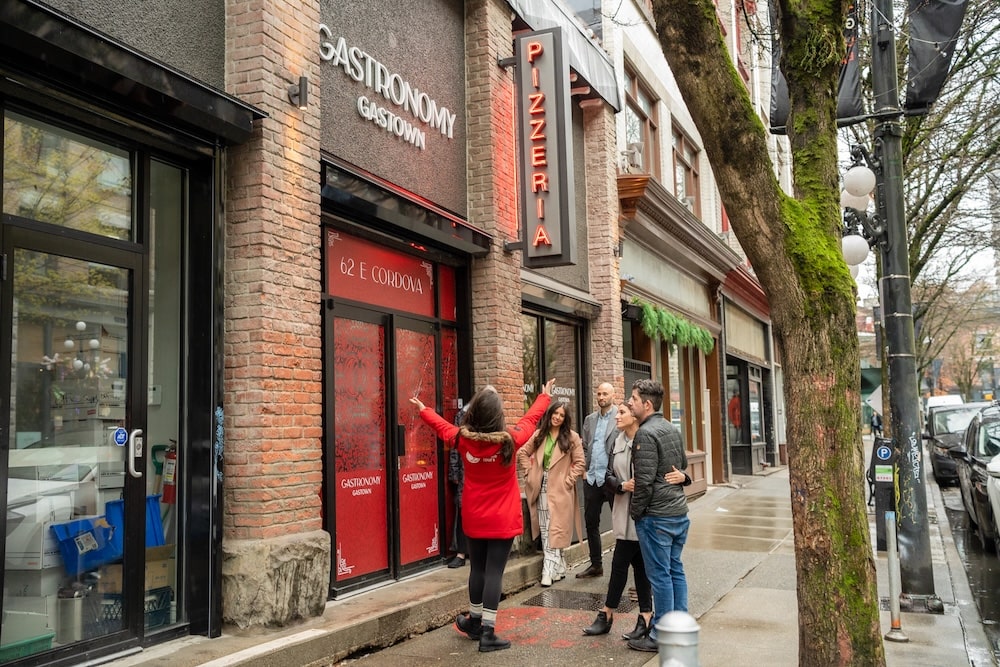 a tour guide standing in front of the restaurant Gastronomic Gastown in Vancouver with her group of guests on a food tour