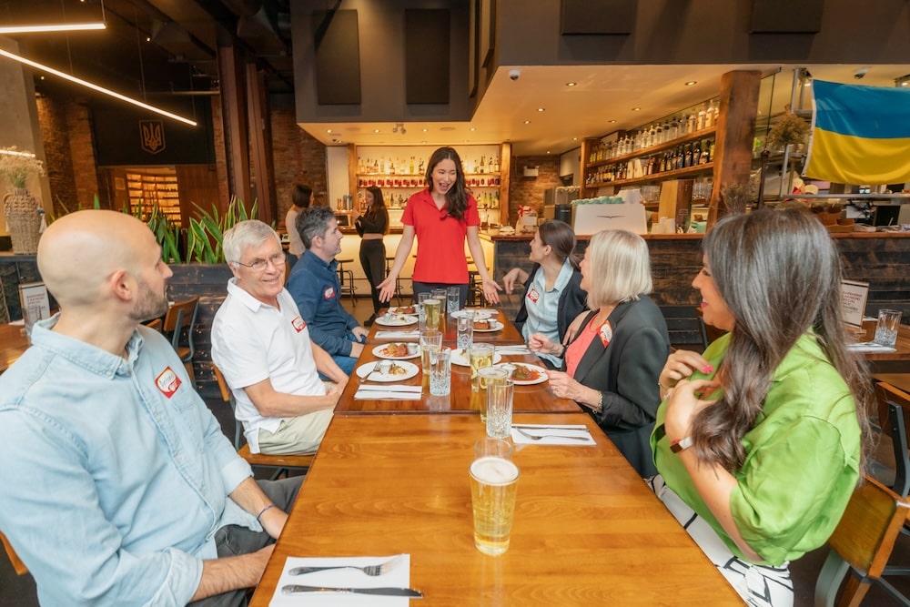 a Vancouver Foodie Tour guide standing in front of a table in the Kozak Restaurant in Vancouver, with her guests on a food tour seated around and listening to her