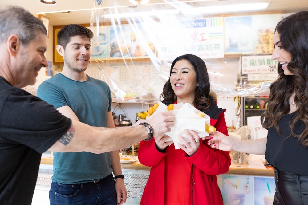 A corporate team of coworkers on a group tour in Vancouver reaching out to their friendly tour guide for delicious-looking tastings of local cuisine during a team-building activity