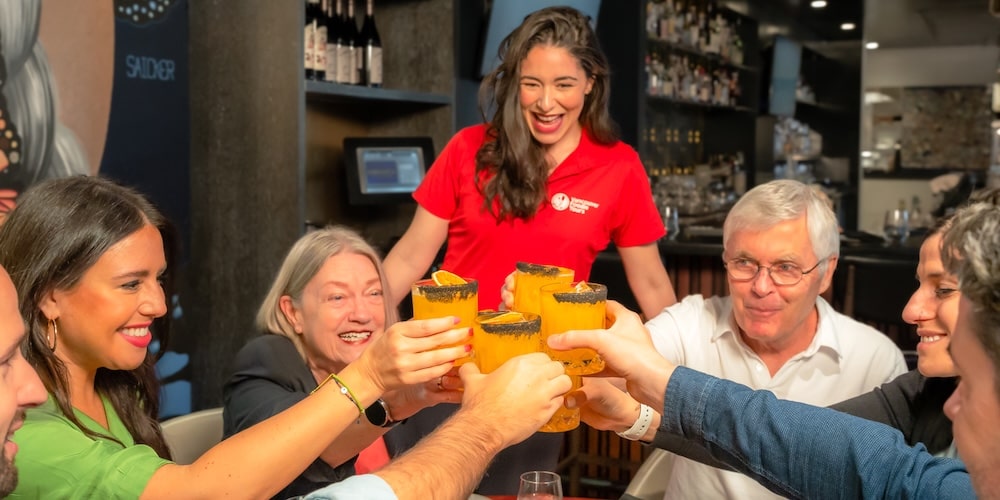 a local tour guide cheering her group of guests on a gastronomic tour in Vancouver's Gastown while they raise their cocktail glasses for a toast together