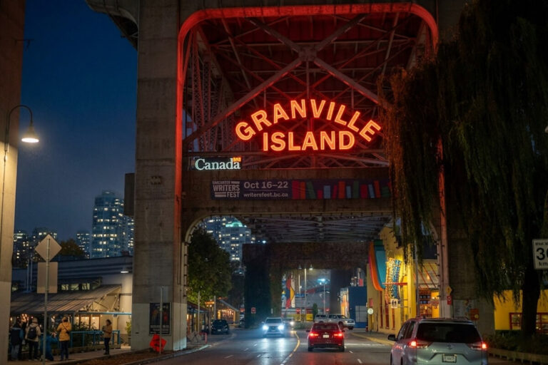 Granville Island sign glowing at night beneath the bridge entrance in Vancouver.