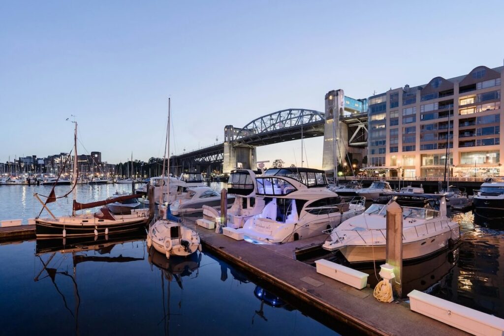 Granville Island marina at dusk with boats and bridge lights reflected on the water.
