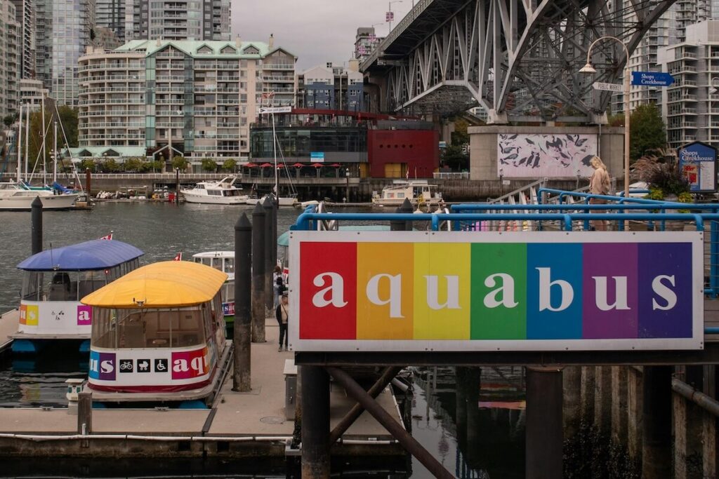Aquabus docked at Granville Island with False Creek waterfront and bridge in the background.