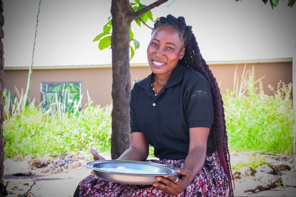 Smiling woman seated outdoors holding a large tray of rice, highlighting access to nutritious food.