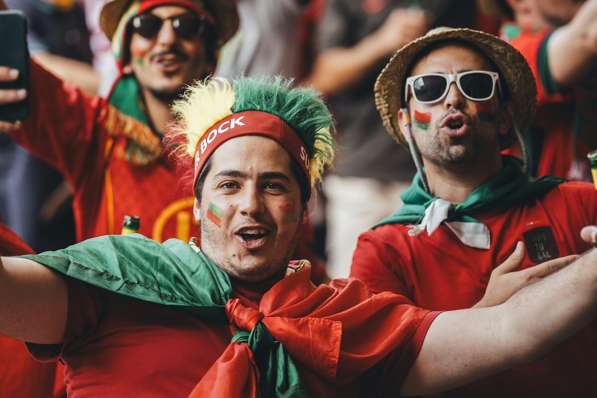 Football fans in red and green outfits cheering in a crowded fan festival atmosphere.