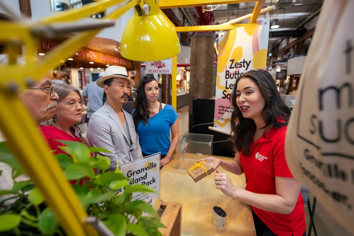 Vancouver Foodie Tours guide sharing shopping tips with guests inside Granville Island Public Market.