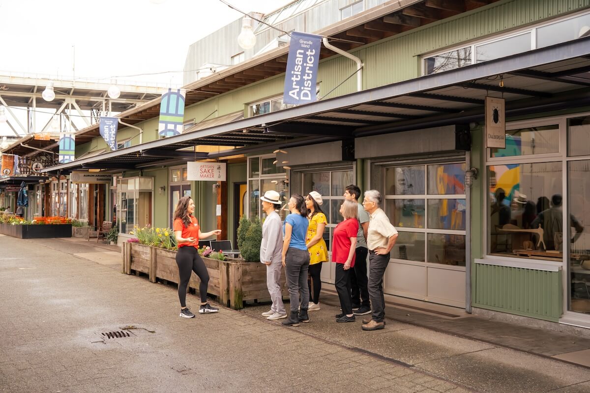 A guide speaking to a small group outside artisan shops in Granville Island’s Artisan District.