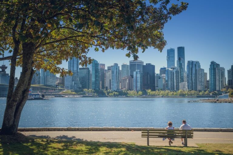Outdoor activities in Vancouver. View of downtown skyline from Stanley Park with people relaxing on a bench