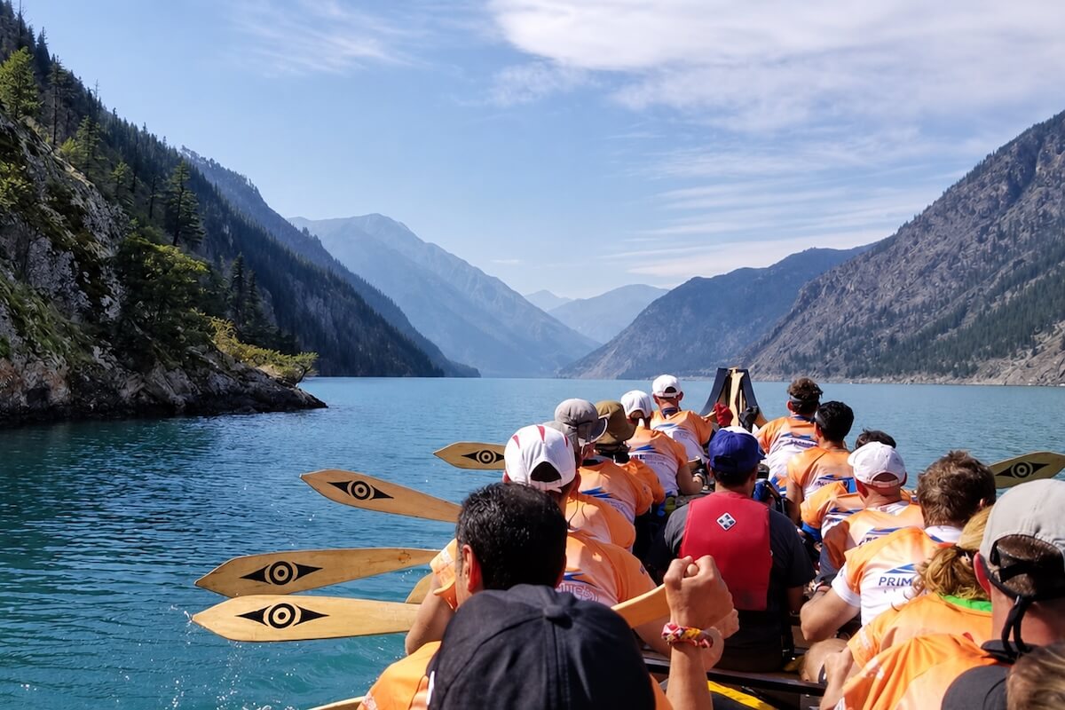 Takaya Tours participants paddling a traditional canoe across a mountain lake in British Columbia.