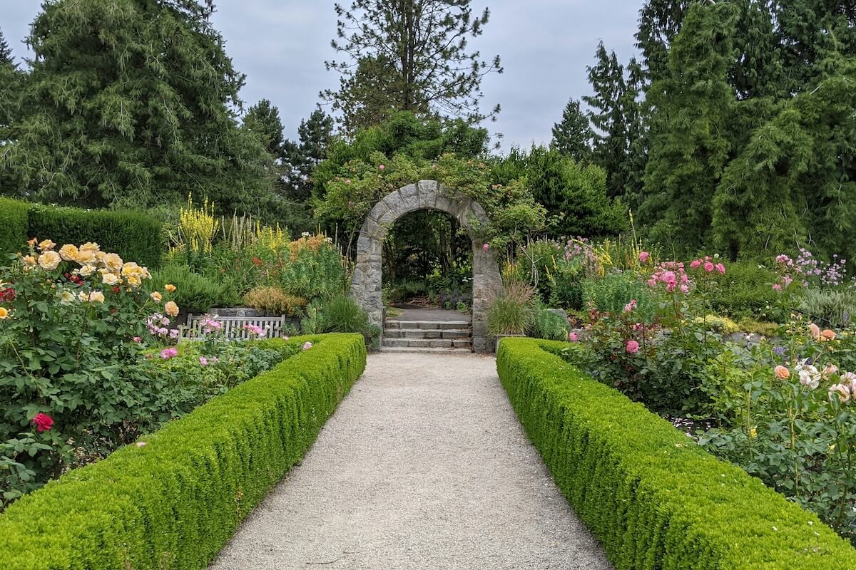 Formal garden path lined with clipped hedges and roses leading to a stone arch at VanDusen Botanical Garden in Vancouver.