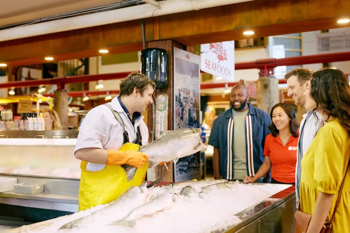 Fishmonger showing a whole salmon to a small tour group at Granville Island Public Market