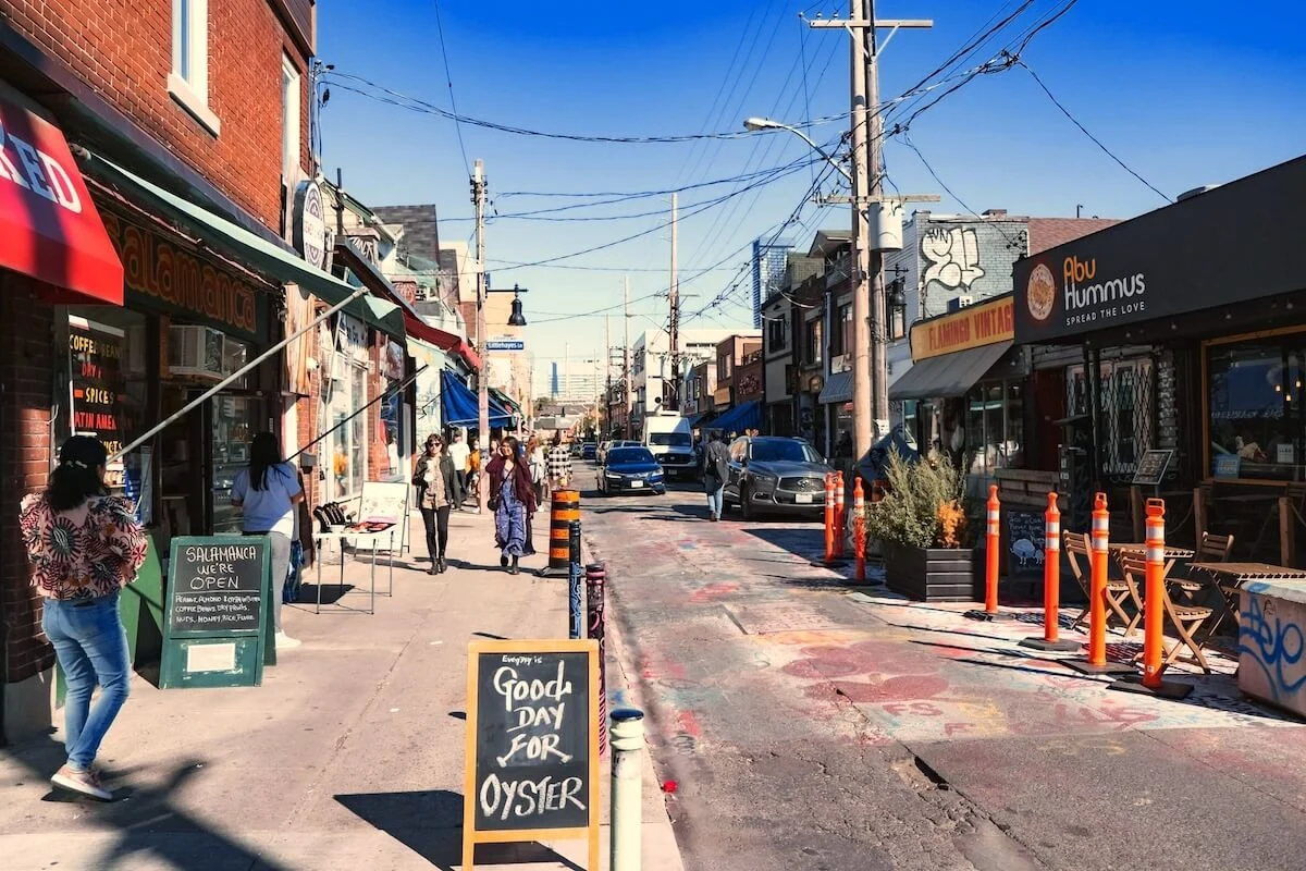 Colourful shopfronts and sidewalk signs along a street in Kensington Market, Toronto