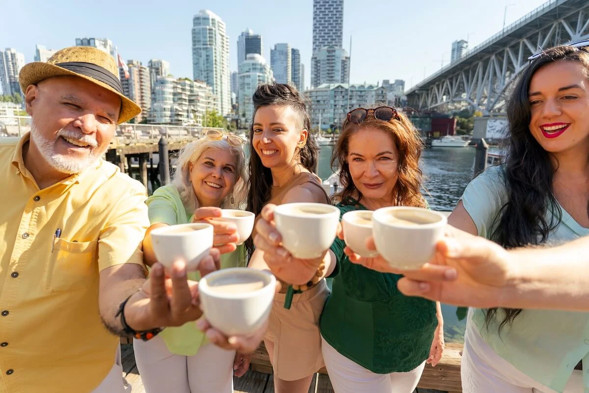 Food tour guests raising tasting cups on Granville Island with downtown Vancouver behind them
